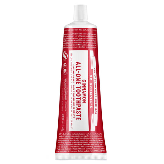 A red and white tube labeled Dr. Bronners All One Cinnamon Toothpaste sits upright, featuring text about fair trade, organic ingredients, and packaging made from sustainable materials [5 oz]