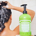 A person shampoos their hair in a shower, with a bottle of Dr. Bronners 4 in 1 Lemongrass Lime Organic Sugar Soap in the foreground. The green bottle emphasizes its versatility for hair, face, body, and hands [24 oz]
