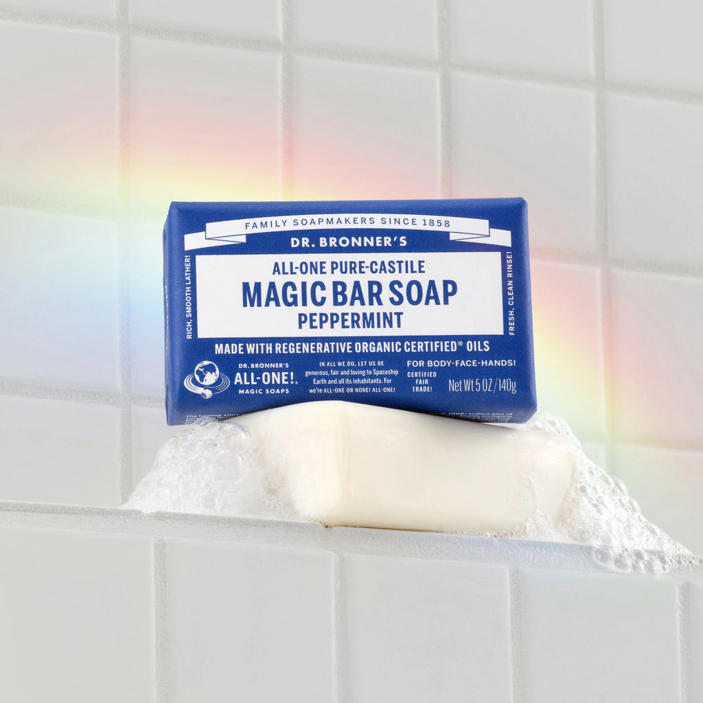 Dr. Bronners Magic Bar Soap, Peppermint, sits on a wet surface, creating suds against a tiled background with a faint rainbow. DR. BRONNERS ALL ONE PURE CASTILE MAGIC BAR SOAP PEPPERMINT. MADE WITH REGENERATIVE ORGANIC CERTIFIED OILS [5 oz]