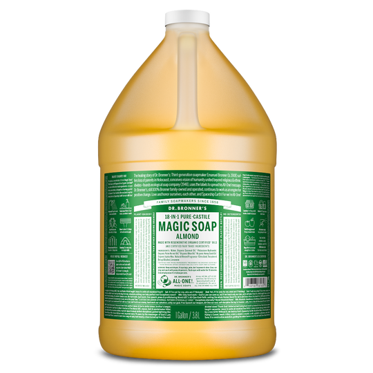 A large, transparent jug filled with a golden liquid features a green label. The text reads Dr. Bronners Magic Soap, 18 in 1 Pure Castile, Almond, 1 Gallon 3.8L. Eco friendly product details are printed below in white [1 Gallon]