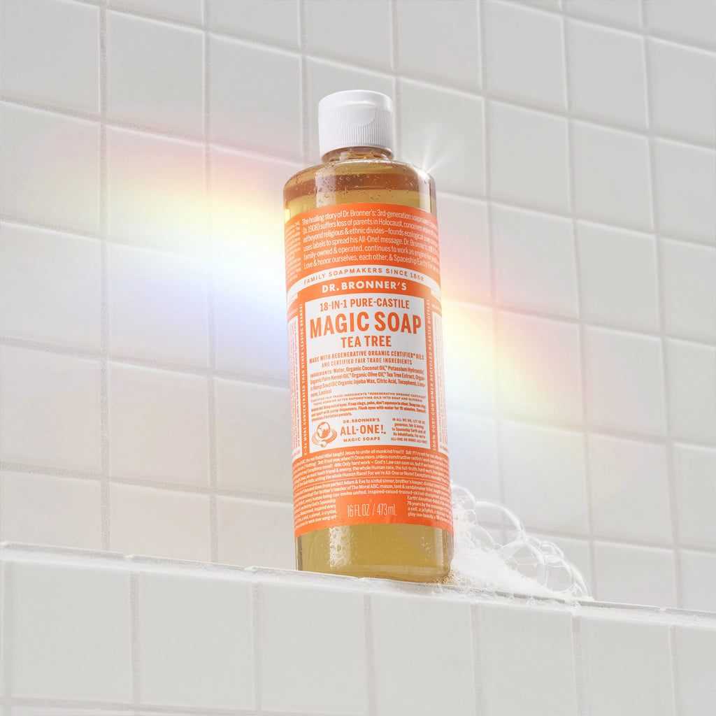 A bottle of Dr. Bronners Citrus Pure Castile Liquid Soap stands on a white tiled shelf, illuminated by a rainbow reflection. Ideal for eco friendly, vegan personal care routines [16 oz]