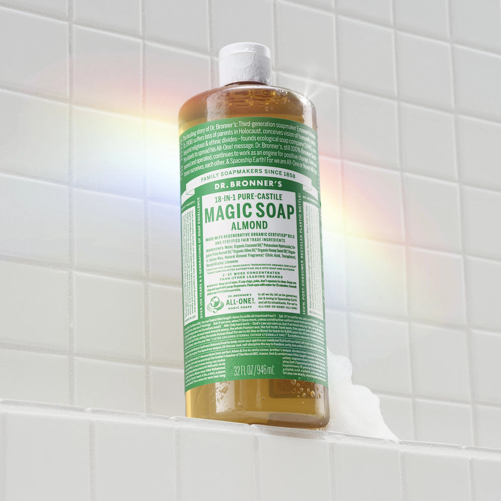 A bottle of Dr. Bronners Pure Castile Soap stands upright on a tiled bathroom shelf, with a rainbow light effect on the tiles. Text reads ALL ONE MAGIC SOAPS DR. BRONNERS PURE CASTILE SOAP DR. BRONNERS ALL ONE FAITH SERVICE SIGHT LOVE ALL ONE OR NONE LET THE ALL ONE VISION LIGHT UP STRONG BRIGHT ALL ONE [32 oz]