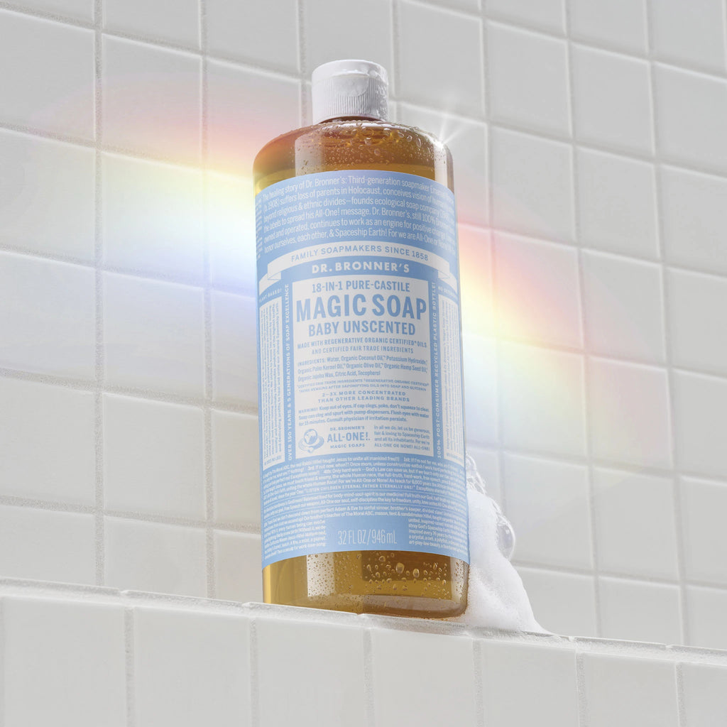 A bottle of Dr. Bronners Baby Unscented Pure Castile Liquid Soap stands vertically on a tiled surface, catching sunlight to create a subtle rainbow effect [32 oz]