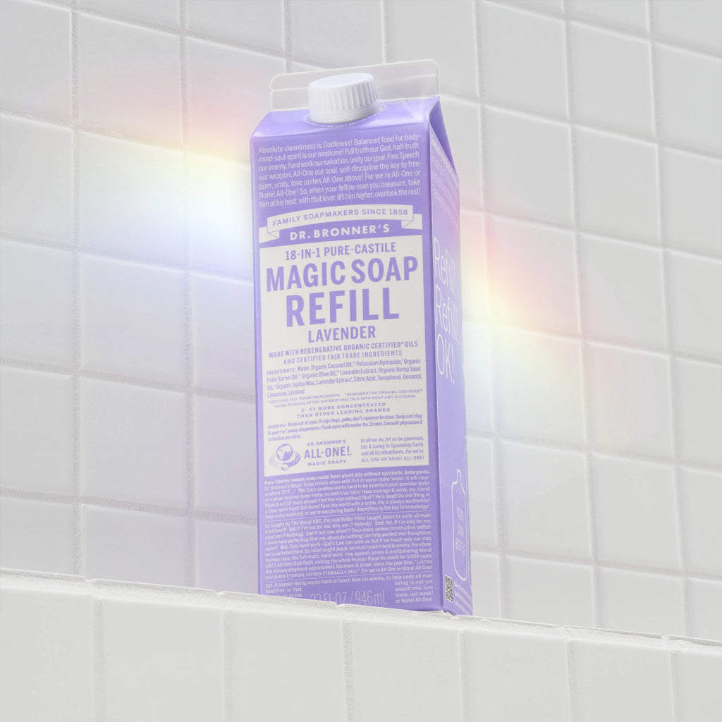 A lavender carton of Dr. Bronners Magic Soap Refill sits on a tiled bathroom shelf. A subtle rainbow reflection dances across the tiles, enhancing the soothing ambiance [32 oz]