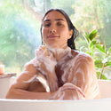 Woman in a bathtub with bubbles, surrounded by greenery [16 oz, 32 oz]