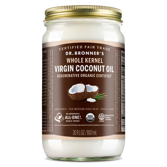 A glass jar with a gold lid contains Dr. Bronners Whole Kernel Virgin Coconut Oil. Its labeled Regenerative Organic Certified and 30 FL OZ 887 mL. The label highlights it as Certified Fair Trade and suitable for medium high heat cooking [30 oz]